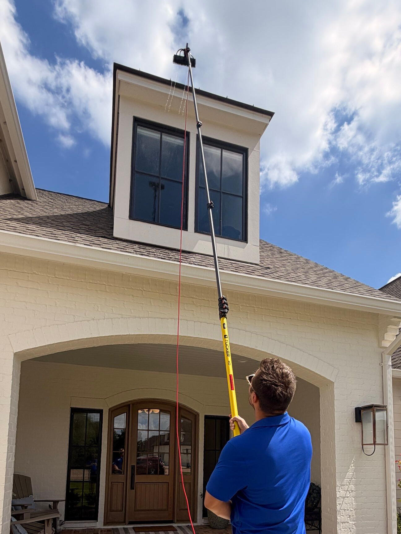 Crew member cleaning second-story windows with a water-fed pole